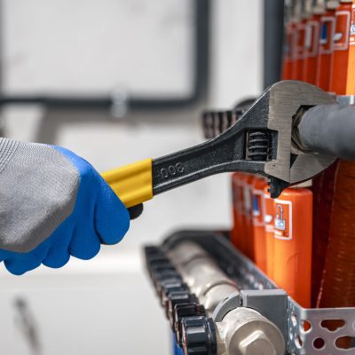 Male hands with a wrench turning off valves. Male hands with a wrench turning off valves. Adjusting heating valves in a residential building. A plumbing and heating technician works.